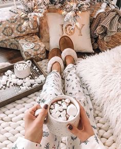 a woman is holding a cup of hot chocolate in front of a decorated christmas tree