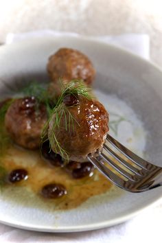 a fork with some meatballs on it in a white bowl and garnished with green sprigs