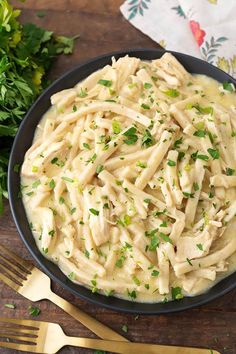 a bowl filled with pasta and parsley on top of a wooden table next to silverware