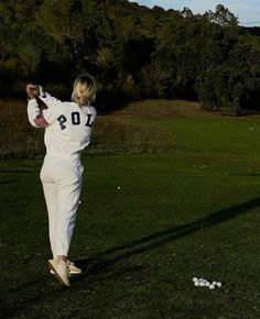 a woman in white is playing golf on the green grass with her back to the camera