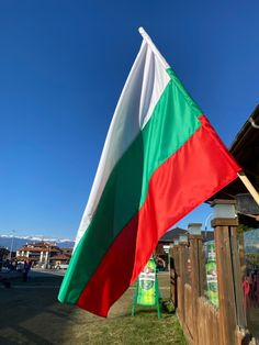 a large flag flying in the wind on top of a green field next to a wooden fence