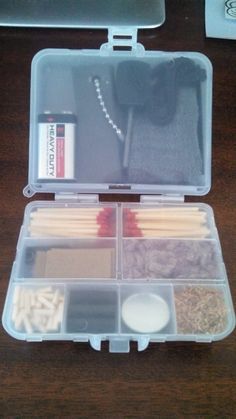 an open plastic box with matches and other items in it on a wooden table next to a computer keyboard