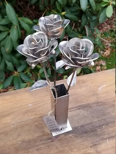 three metal roses in a silver vase on a wooden table