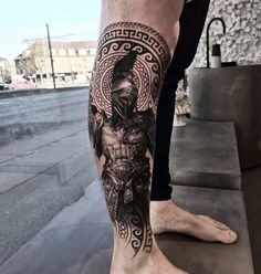 a man's leg with a black and grey tattoo design on the side of his leg