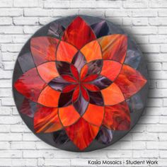 an orange and black flower on a brick wall with the words kasia mosaics student work