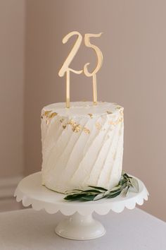 a white cake sitting on top of a table with a wooden number twenty five candle