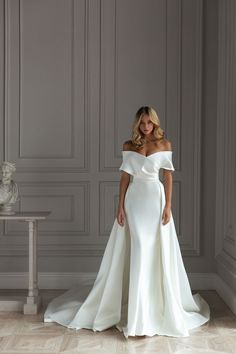 a woman in a white wedding dress standing next to a table with a vase on it