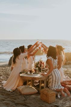 a group of women sitting on top of a beach next to each other holding wine glasses