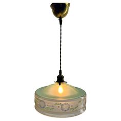 a glass hanging light with a black cord attached to the bottom and an illuminated bulb above it