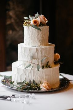 a three tiered cake with flowers and greenery on the top is ready to be cut