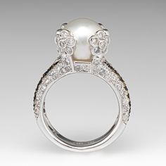 a white pearl and diamond ring on a gray background with the center stone surrounded by smaller diamonds