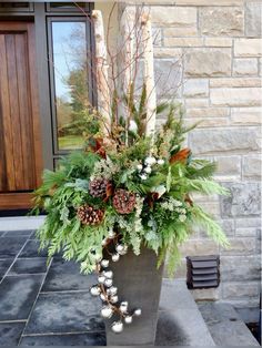 a vase filled with flowers and greenery sitting on top of a stone floor next to a door