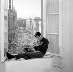 a man sitting on top of a window sill next to a cityscape