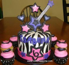 a birthday cake with cupcakes and an electric guitar on the top is sitting on a table