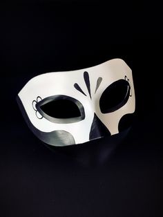 a white mask with black and grey designs on the face, against a black background