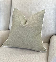 a light gray pillow sitting on top of a beige couch next to a white chair