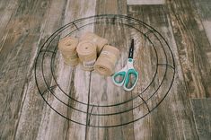 yarn, scissors and twine are sitting on a round wire rack with wood flooring