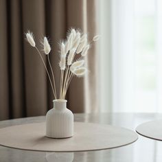 a vase with some white flowers in it on a table next to a curtained window