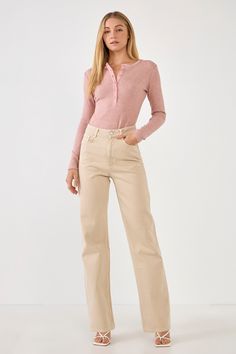 a woman standing in front of a white background wearing beige pants and a pink sweater