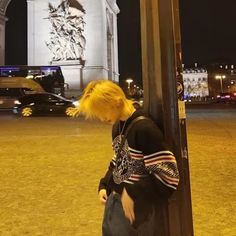 a person with yellow hair leaning against a pole