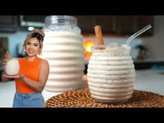 a woman is holding two desserts in front of some large vases with strawberries on them