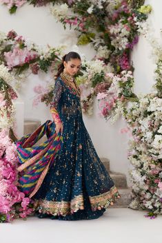 a woman standing in front of flowers wearing a blue lehenga with gold and pink accents