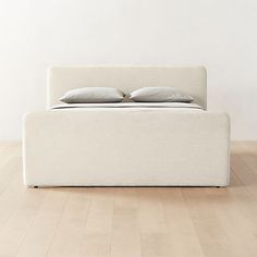 a bed sitting on top of a hard wood floor next to a white wall with two pillows