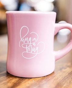 a pink coffee mug with the words mama on it sitting on a wooden counter top