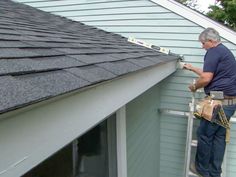 a man on a ladder painting the side of a house's shingled roof