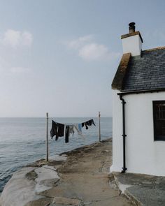 clothes hanging out to dry by the water's edge near a white house with black shingles