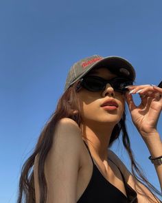 a woman wearing sunglasses and a hat holding a cell phone up to her ear with the sky in the background