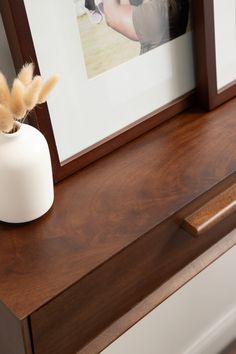 a white vase sitting on top of a wooden table next to a framed photo and feather