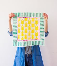 a person holding up a piece of paper with yellow and green designs on it in front of their face