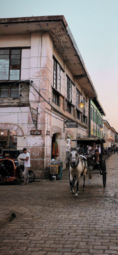 a horse pulling a cart down a street next to tall buildings and people on the sidewalk