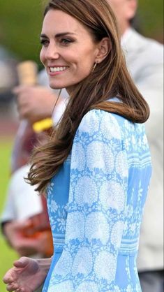 the duke and duchess of cambridge smile as they walk through an open field with other people