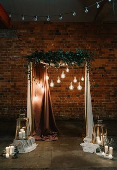 an outdoor ceremony with candles and greenery on the ground, surrounded by lights that are hanging from the ceiling