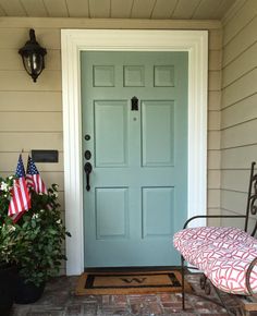 a blue front door on a house with american flags and potted plants in the foreground