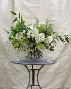 a vase filled with white and green flowers on top of a small round table next to a wall