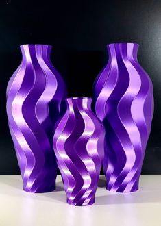 two purple vases sitting next to each other on a white counter top in front of a black background