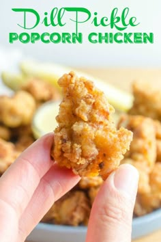 a hand holding up a piece of fried chicken in front of a bowl of lemon wedges