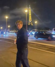 a man is standing on the sidewalk in front of some cars and street lights at night