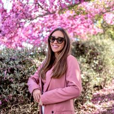 a woman standing in front of a tree with pink flowers