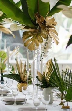 an arrangement of flowers and greenery in vases on a white table cloth with place settings