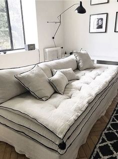 a white couch with pillows on it in front of a window and pictures on the wall