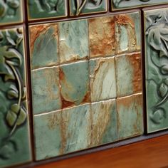 some tiles that are on top of a wooden table in front of a wall with green and brown designs