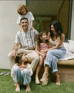 a family sitting on the grass in front of their house with one child and two adults