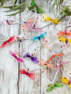 several colorful butterflies are hanging from string on a white wooden surface with green leaves and beads