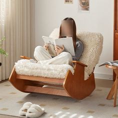 a woman sitting in a rocking chair reading a book while wearing white pants and slippers