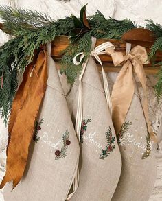 three christmas stockings hanging from a mantle with pine cones and evergreen leaves on them, decorated with ribbon