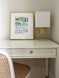 a white desk with a lamp on top of it next to a painting and chair